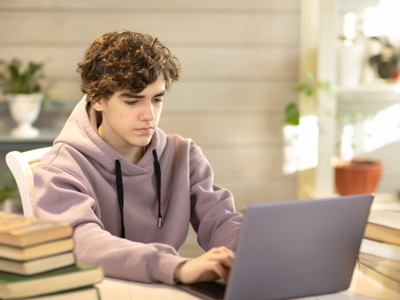 Adolescente utilizando un simulador COMIPEMS en su computadora junto a libros de estudio.