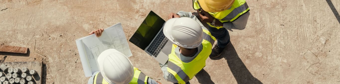 Equipo de ingenieros civiles revisando planos y laptop en construcción