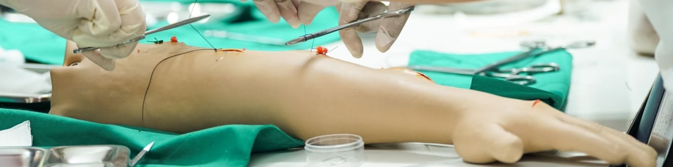 Práctica de suturas en simulador clínico de extremidad como parte del entrenamiento en procedimientos médicos.