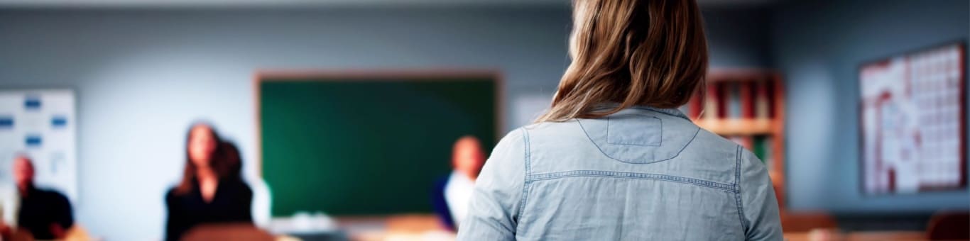 Profesional de la educación hablando frente a un grupo en un salón, representando capacitación y gestión educativa.