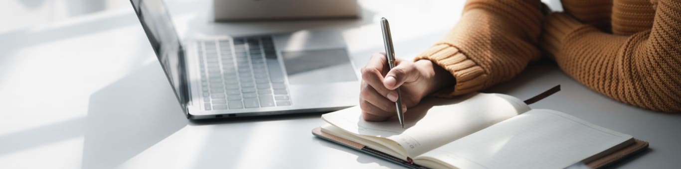 Manos escribiendo en un cuaderno sobre un escritorio, enfoque en estudio y toma de apuntes.