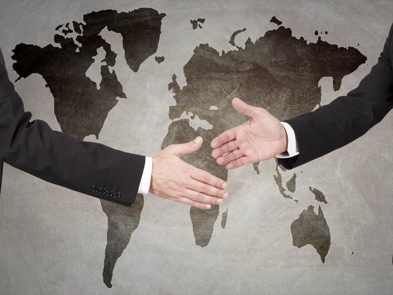 Licenciados en relaciones internacionales dándose la mano frente a un mapa mundial. 